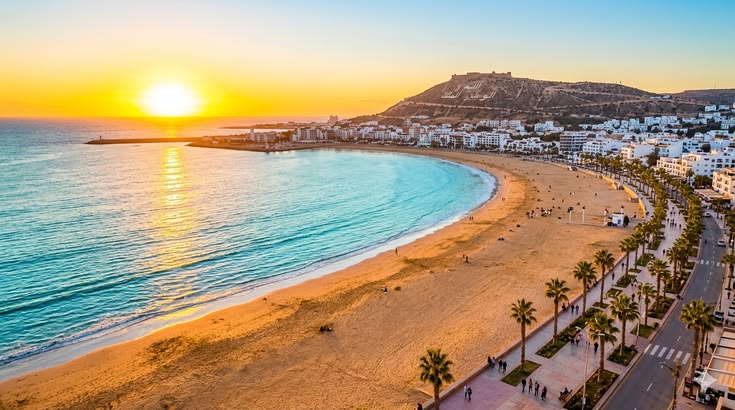 A stunning sunset casts vibrant colors over a serene beach in Spain, with gentle waves lapping at the shore.