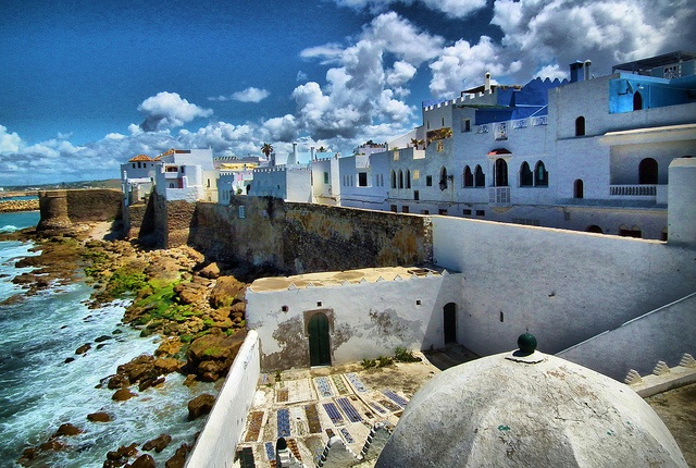 Coastal view of Asilah, Morocco, featuring charming blue and white buildings against a clear sky and ocean backdrop.