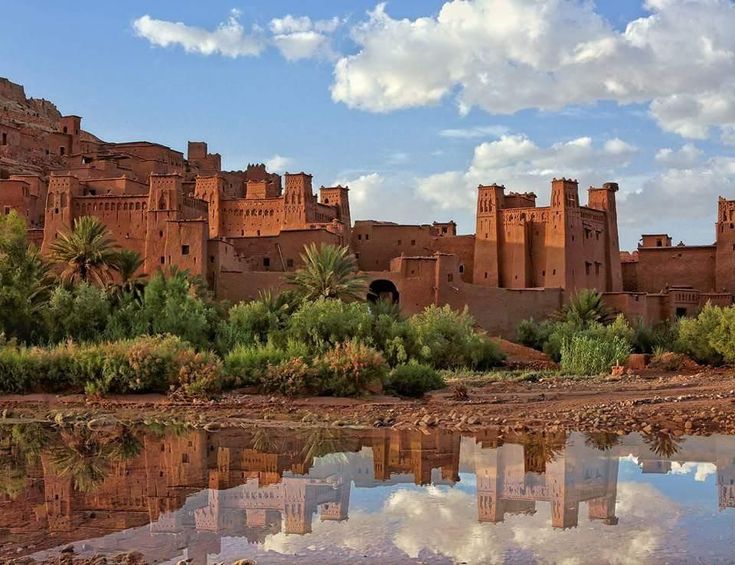 Scenic view of Tinghir, Morocco, with the city beautifully reflected in calm water, showcasing its vibrant architecture.